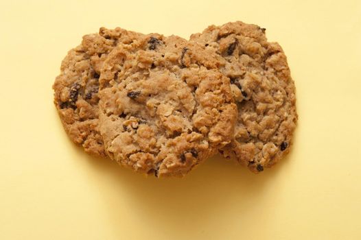 Overhead view of a pile of crunchy raisin cookies on a pale yellow background with copyspace