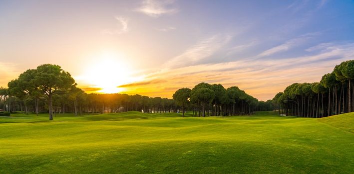 Golf course at sunset with beautiful sky. Scenic panoramic view of golf fairway