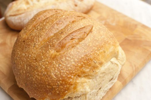 Round loaf of fresh rustic bread with a crusty top on a wooden bread board, close up view from above