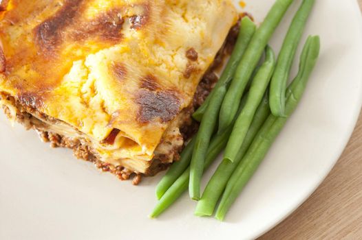 Close up Healthy Fresh Cooked Italian Lasagne Food on a White Plate with Green Beans on the Side.