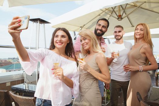 Group of friends taking selfies on a smart phone together during rooftop party