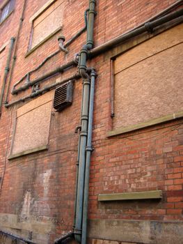 Old metal pipes attached to the exterior brickwork of a building with a rusted airconditioning duct