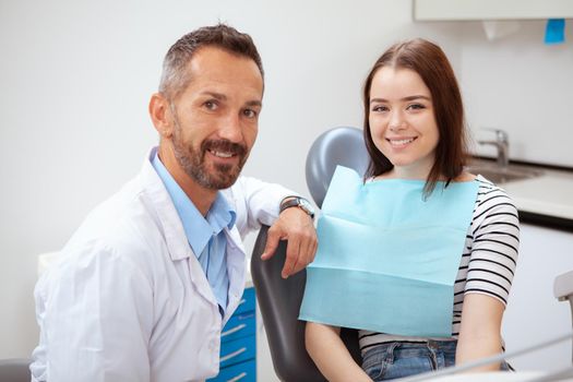 Handsome mature male dentist and his charming female patient smiling to the camera after medical examination