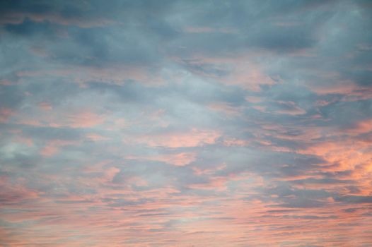 Delicate diffuse pink sunset lighting up a heavy cloud cover from below as the sun sinks below the horizon in a cloudscape and nature background
