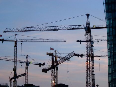 Group of heavy duty cranes on a construction site silhouetted against an evening sky conceptual of urban expansion and development