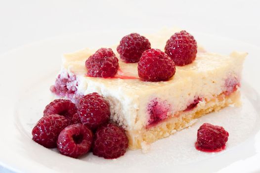 Slice of freshly baked ricotta cheesecake with raspberries served on a plate over a white background