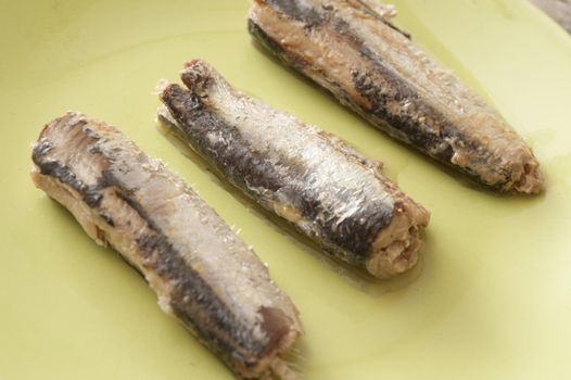 Three canned sardines on a yellow plate arranged separately in a neat row, close up high angle view