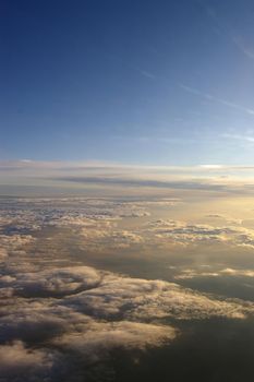 a view of clouds below from a high altitude aircraft as the sun sets