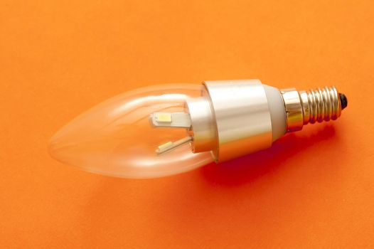 LED candle shaped light bulb with a screw fitting on an orange background showing diode detail