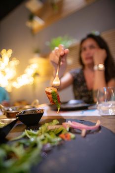 A hungry Hispanic girl is sitting in a restaurant and eating a delicious dinner alone.