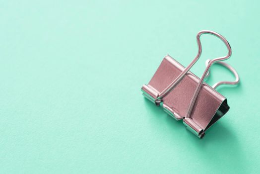 Single metal bulldog clip against mint background