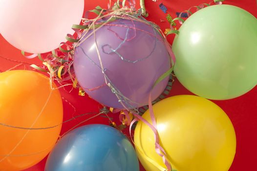 Overhead background view of a bunch of colorful party balloons and streamers for use as celebration decorations on red