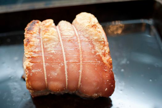Roasting pork in the oven with a close up view of a cut of rolled pork with crisp crackling in a grill pan
