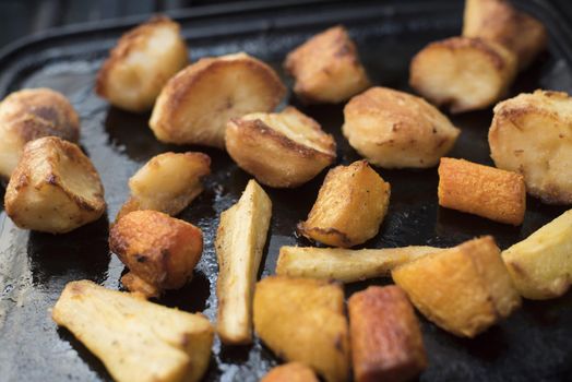 Roasting slices of potato and parsnips on a pan, viewed in close-up from high angle