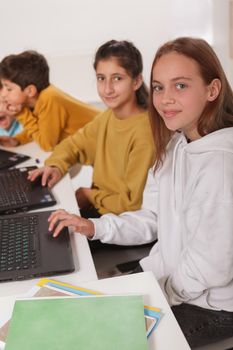 Vertical shot of teen girls students smiling to the camera while working on computers at school