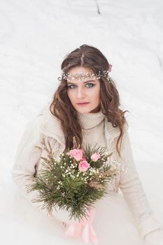 Beautiful bride in a white dress with a bouquet in a snow-covered winter forest. Portrait of the bride in nature.