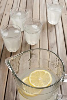 Fresh cold homemade lemonade served in four tumblers from a jug with fresh sliced lemon on a wooden picnic table, high angle close up view