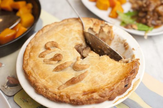 Tasty freshly baked meat pie with pastry crust served with vegetables with a spoon in the dish and portion missing