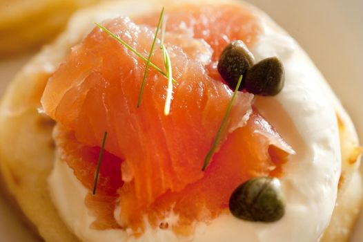 Selective focus macro close up on raw pink salmon meat with capers and herbs on little pancake