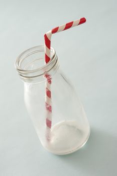 Consumed empty glass milk bottle with colorful red and white striped plastic straw over grey in a healthy diet concept