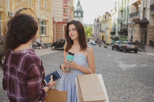 Young women talking on the city streets after shopping, copy space. Beautiful woman smiling, talking to her friend while sightseeing and shopping during summer vacation