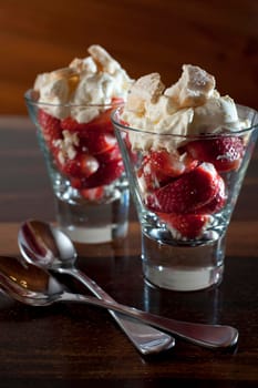 Two delicious fresh strawberries and whipped cream desserts served in tall glasses with spoons over a dark background