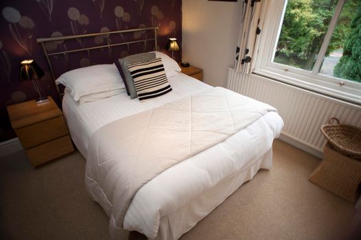 Modern bedroom interior with a comfortable double bed and bedside tables alongside a window and radiator with a garden view