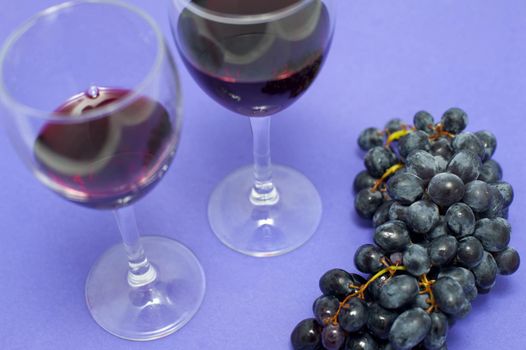 Two glasses of red wine with a bunch of fresh grapes in a viticulture and agriculture concept over a purple background