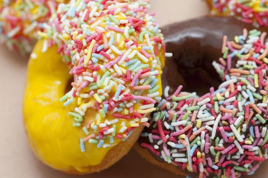 Batch of freshly baked glazed doughnuts or donuts with chocolate and lemon icing dipped in colorful sprinkles on display in a bakery