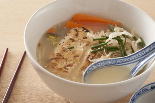 Asian soup made of grilled meat in clear broth, carrot sticks, chives, sliced onions and with a decorative ceramic spoon