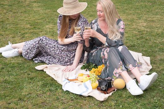 a two young women in a summer long dresses is resting on a picnic, a Blanket with cheese plate and fruits, rest from worries and household chores, parks and recreation areas,.High quality photo
