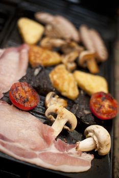 Full cooked English breakfast with bacon rashers, mushrooms, tomato French toast and sausages on a griddle with shallow dof