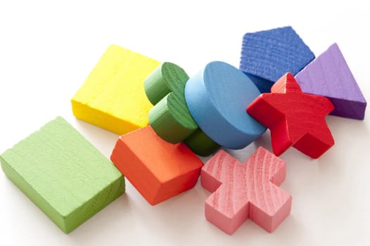 Colorful educational wooden toys in different basic geometric shapes heaped on a white background in a close up high angle view