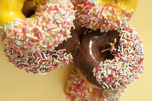 Glazed ring donuts with multicolored sprinkles and colorful lemon and orange or rich chocolate icing