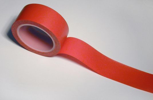 Red insulating tape with unrolled end viewed in close-up on white background