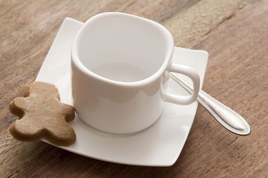 Clean white coffee cup and saucer with a silver teaspoon and gingerbread man cookie on a wooden table