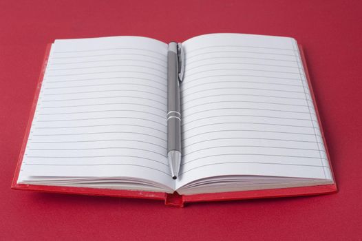 Red notebook and ball pen on red background