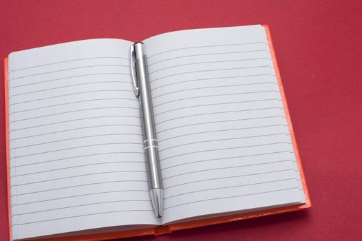 Lined blank notebook opened to the centre with a silver metallic ballpoint pen