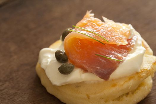 Gourmet appetizer with smoked salmon, capers and cream cheese served on a blini on a wooden table