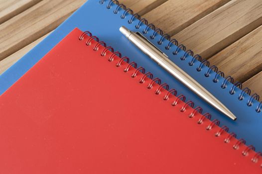 Close up Spiral Blue and Red Office Notebooks with Silver Ballpoint Pen on Top Placed on the Wooden Table.