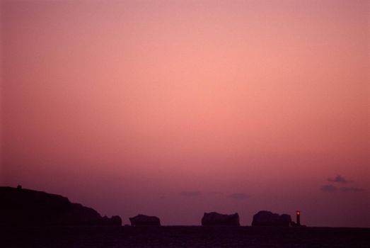 The Needles, a set of chalk stacks rising from the ocean off the Isle of Wight, at dusk with a colorful mauve sky