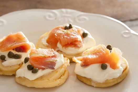 Close up on four salmon caper blinis with cream cheese and capers on white plate