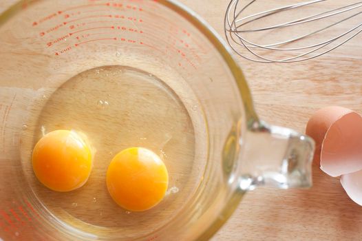 Overhead view of two healthy yellow egg yolks broken into the bottom of a clear glass measuring jug on a kitchen counter to be used as a breakfast or baking ingredient