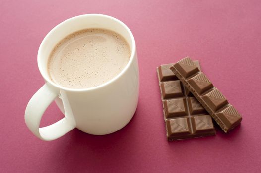 Delicious mug of hot chocolate drink with a partial bar of chocolate alongside used as an ingredient, high angle view over red