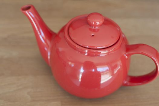 Red ceramic teapot with a bulbous form and shiny glaze on a wooden table, high angle view