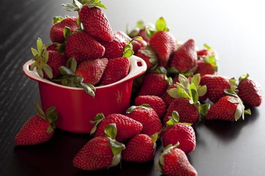Fresh juicy ripe red strawberries overflowing from a small red ceramic ramekin ready for a tasty vegetarian snack or delicious dessert