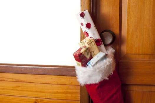 Red Christmas stocking filled with small gifts hanging from a wooden door to celebrate the holiday season, copy space for your greeting