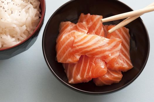 Close up view on raw pink salmon pices in little bowl with wooden chopsticks and herbed white rice