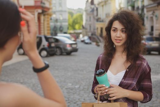 Two young women talking, enjoying warm day, wandering in the city. Lovely woman smiling at her friend while talking on city streets