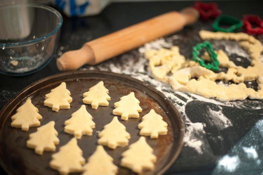 Baking homemade Christmas cookies with pastry cut out in the shape of traditional Christmas trees arranged on a baking tray to go into the oven